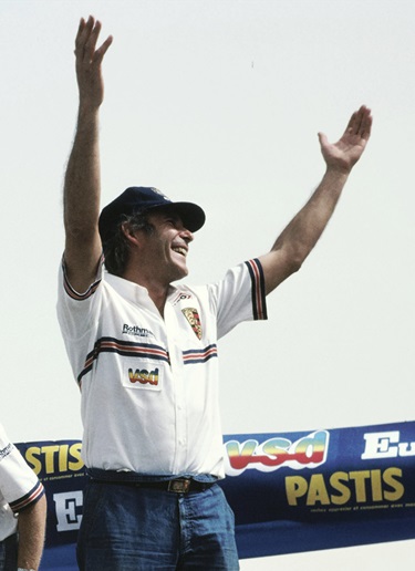 René Metge is seen standing at the finish line and celebrates with his hands in the air.