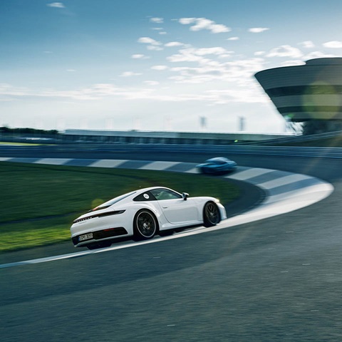 White Porsche 911 drives on race track in the background Porsche Experience Center Leipzig