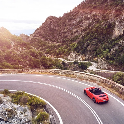 From birds perspective red Porsche Cabriolet drives in a curve