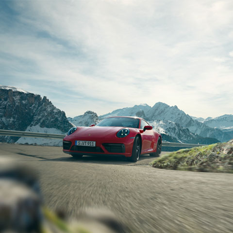 Red 911 Carrera GTS takes corner on Alpine road
