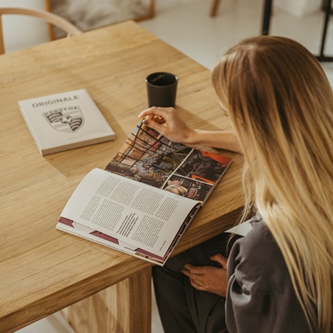 Woman reading Porsche ORIGINALE 08 magazine on a wooden table
