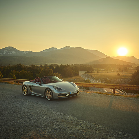 Silver Boxster 25 years lit by setting sun, mountains behind