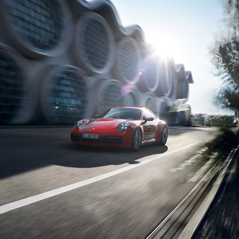 Red Porsche 911 driving past blurred building with large, circular windows