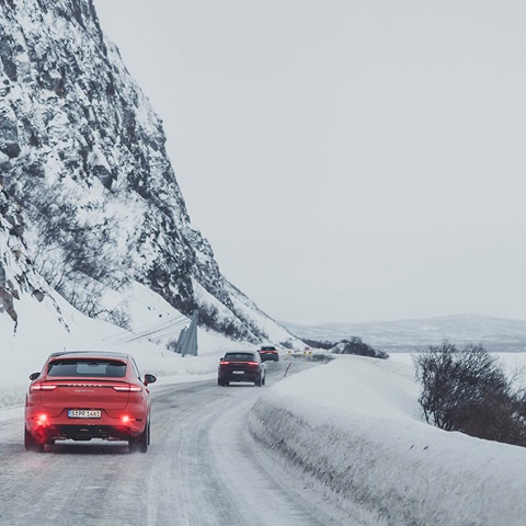 Red Porsche Cayenne in the foreground, two Cayenne in the background are driving in snowy landscape