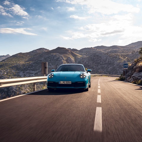 Blue Porsche is driving in front of mountains