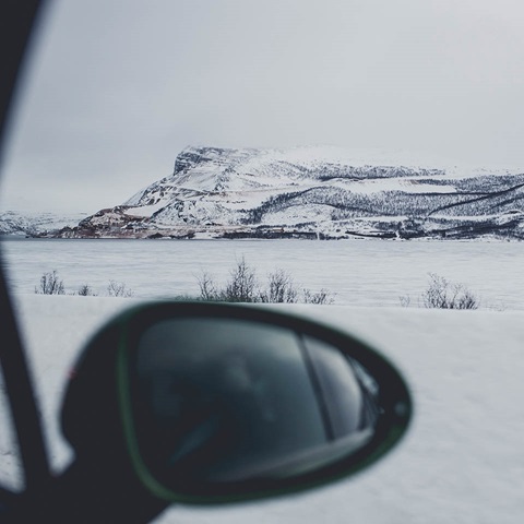 Photo from side mirror of a car. In the background snow-covered hills