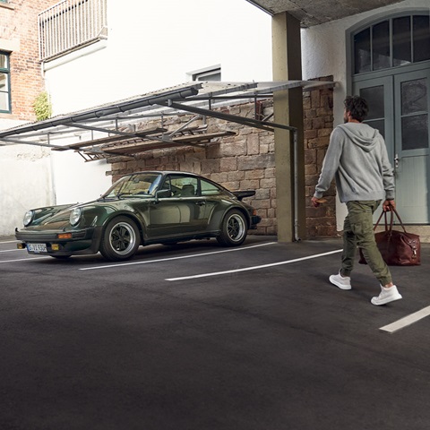 Man walking to green Porsche 911 holding a bag