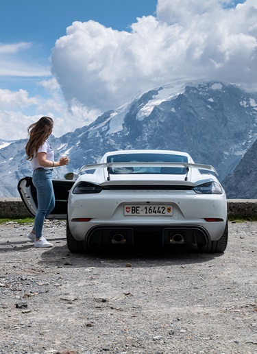 Woman with white Porsche 718 Cayman GT4 in snow-capped mountains