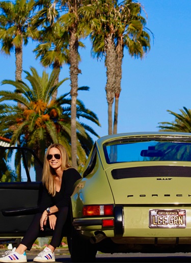 Woman sits in green Porsche 911 with palm trees behind