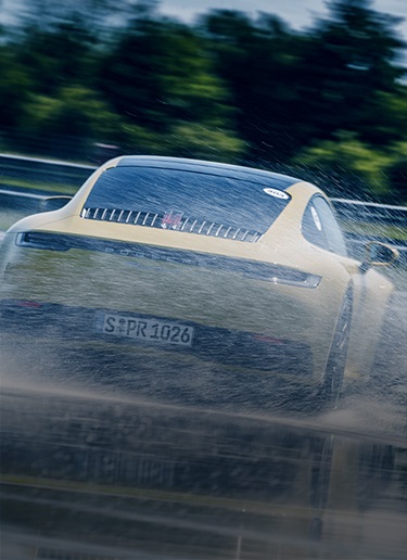 Rear view of yellow 911 drifting on wet track
