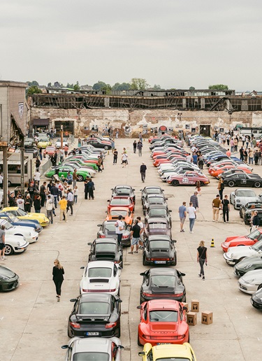 Large line-up of classic Porsche sportscars at show, urban location