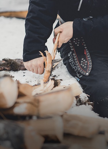 Person whittling stick in the snow with a puukko knife